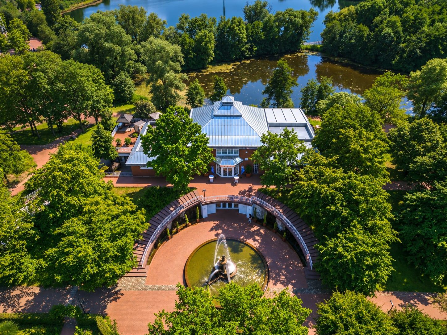 Luftbild des Deichgraf im Südpark: das Haus mit Zinkdach zwischen Bäumen und Wasser, davor der Vorplatz mit Springbrunnen