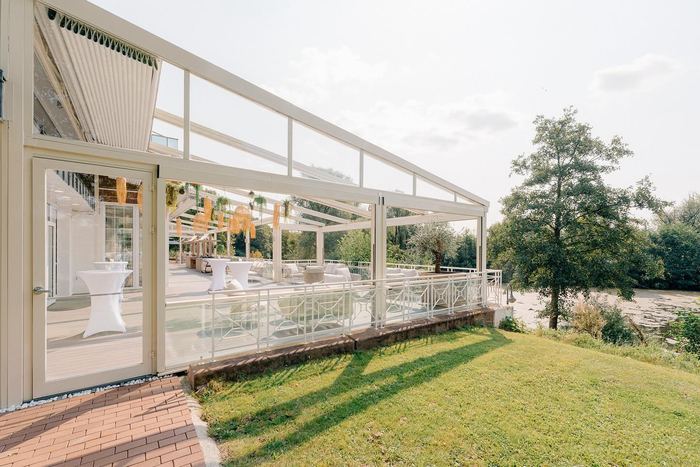 Die überdachte Terrasse mit Wintergarten des Deichgraf von der Rasenseite, rechts Bäume und der Park
