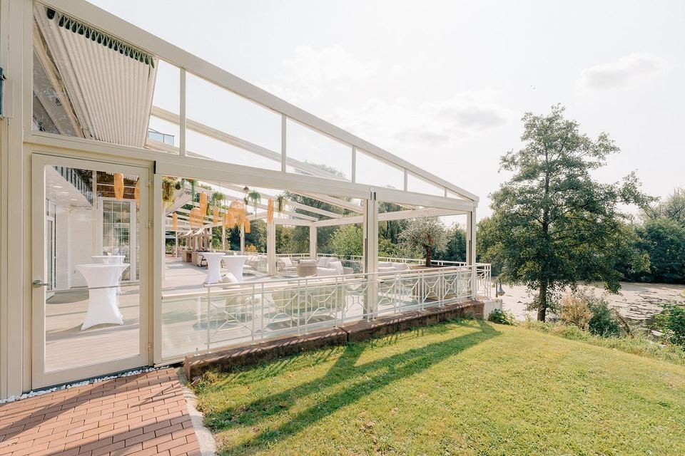 Die überdachte Terrasse mit Wintergarten des Deichgraf von der Rasenseite, rechts Bäume und der Park