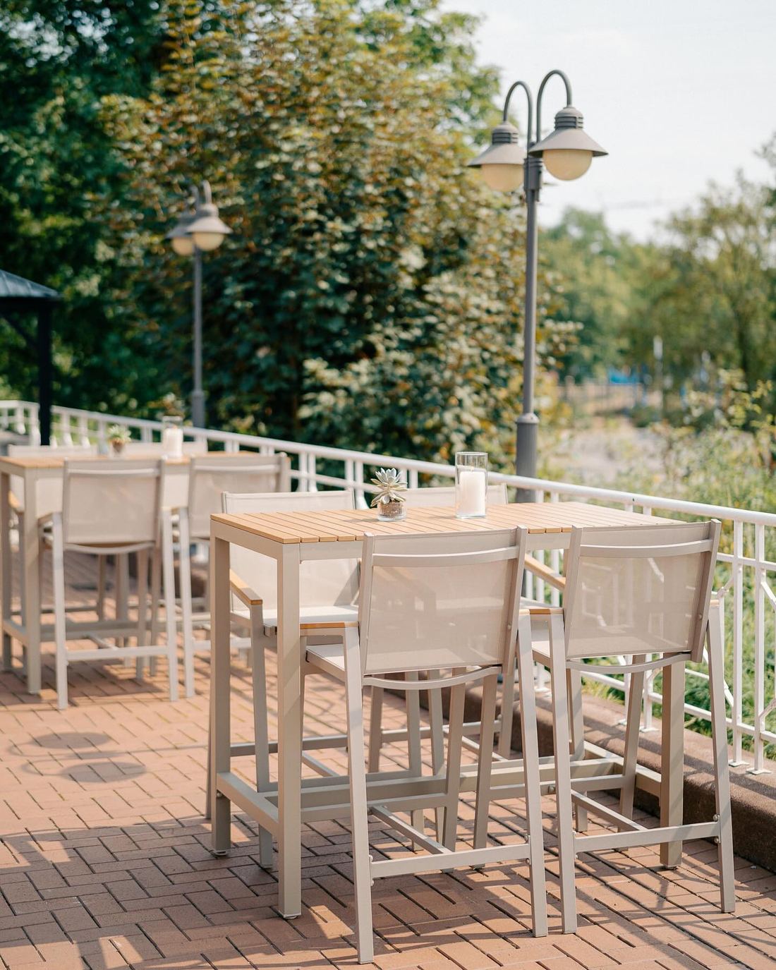 Hohe Tische mit Barhockern auf der Terrasse des Deichgraf, Backsteinpflaster und Laternen im Grünen