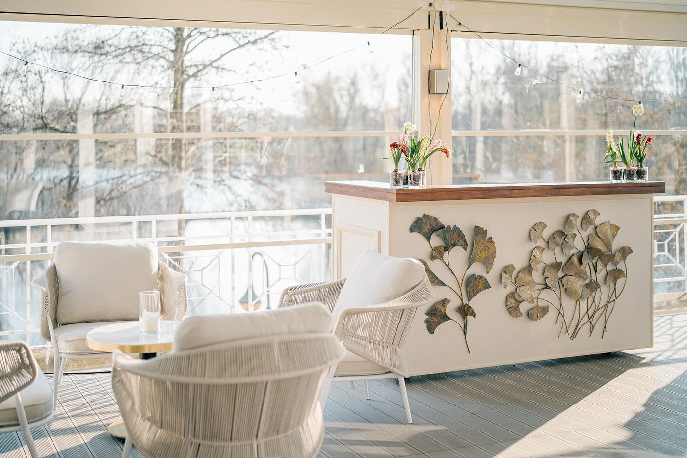 Loungemöbel und eine Bar mit Blattdekor im Wintergarten des Deichgraf, durch die Fenster der Südpark