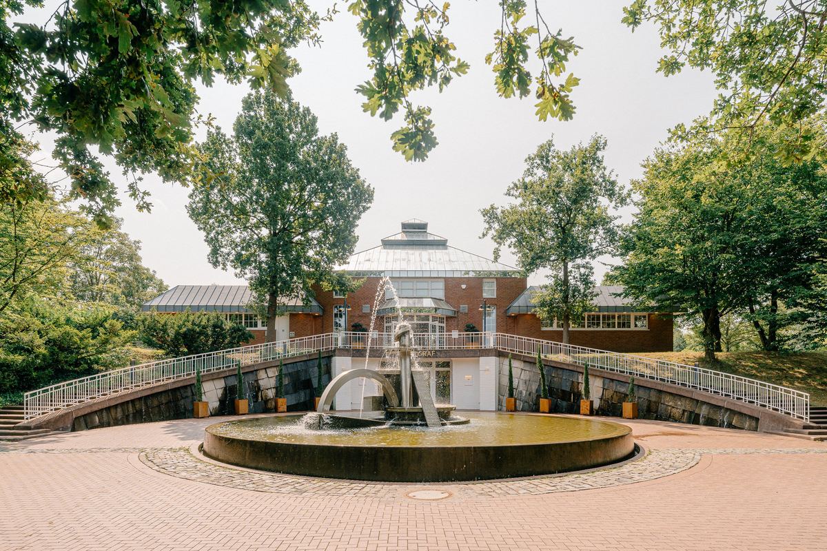 Vorplatz mit Springbrunnen und die Frontansicht des Deichgraf zwischen Bäumen im Südpark